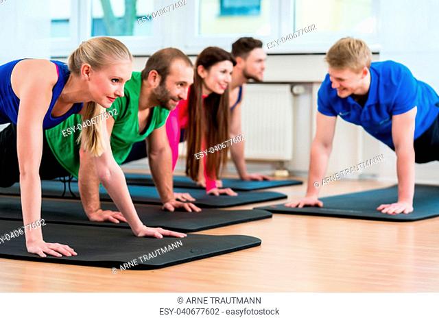 Men and women during floor exercises on yoga mats using medicine balls in gym