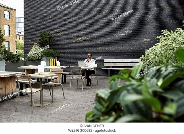 Empresaria pensativa sentado con un portátil en la terraza de la azotea de una cafetería