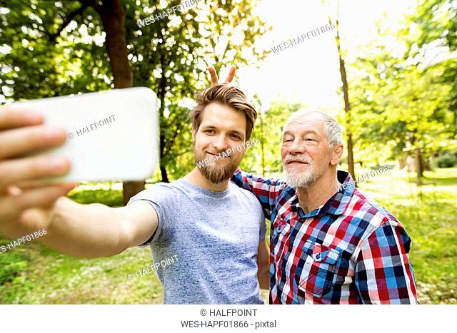 Portrait of senior father and his adult son taking selfie in a park