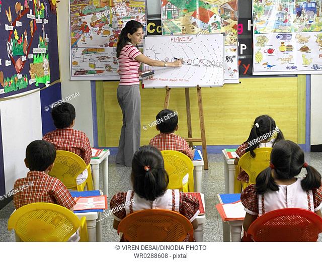 South Asian Indian teacher showing picture on board to children in nursery school MR