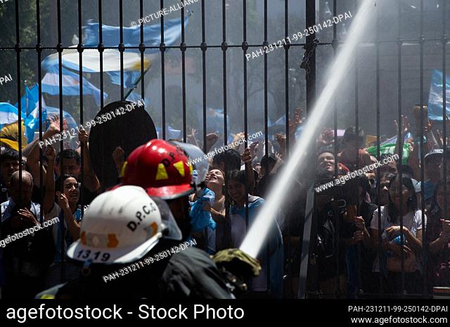 10 December 2023, Argentina, Buenos Aires: People are sprayed with water by the fire department as they wait in front of the government palace in very high...