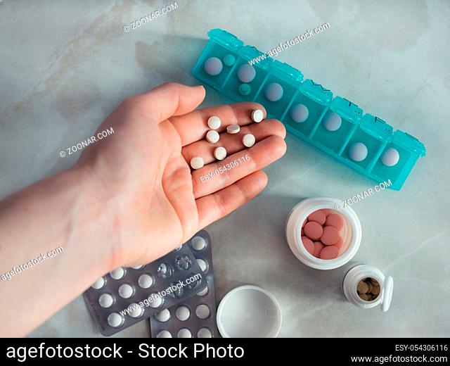 Hand with pills and pillbox. Top view of seven day pill box with pills. Green pill-box over light marble table. Open pill box and open boxes with pills or...