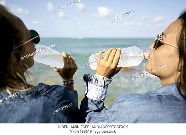 Two women sitting at beach drinking water from plastic bottles, Chersonissos, Crete, Greece