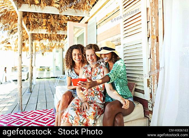 Happy mother and adult daughters taking selfie on beach hut patio