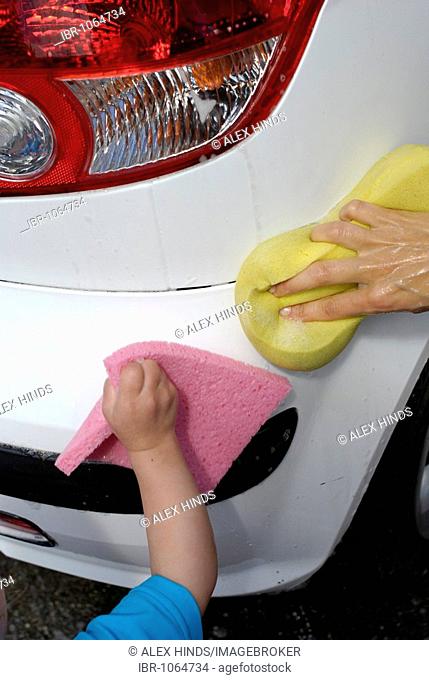 Two year old girl helping her mother to clean the family car