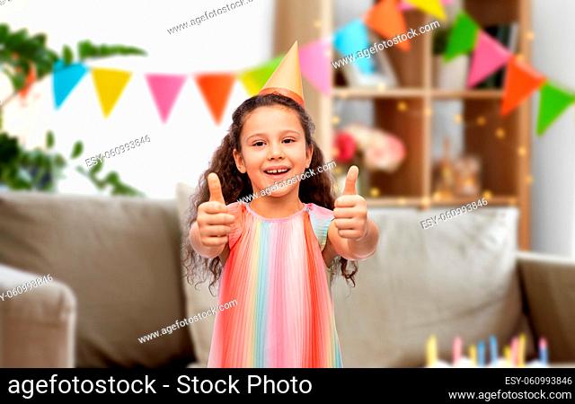 happy girl in birthday party hat showing thumbs up