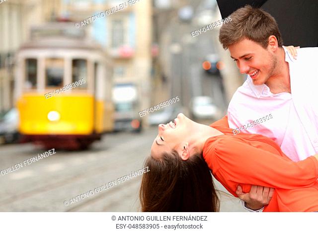 Funny casual couple flirting and joking in the street under an umbrella in a rainy day with a vintage yellow tram in the background