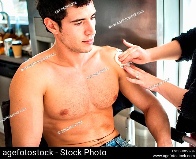 Crop female wiping patch with cotton pad while taking care of shirtless guy inside small room near door