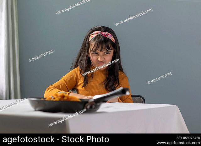 A YOUNG GIRL EXPRESSING UNHAPPINESS OVER FOOD KEPT ON TABLE