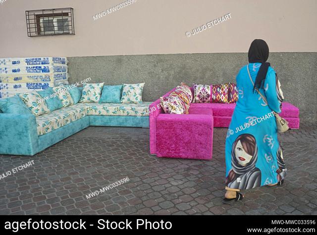 Woman walks past a furniture stall in a market place in Essaouira, Morocco