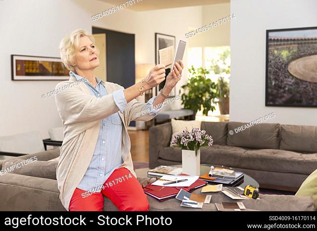 Mature Caucasian female designer working from home, sitting on back of couch with fabric swatches and notes laid out around her