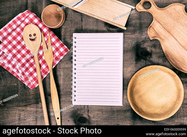 open notepad with wooden kitchen objects on a brown background, top view
