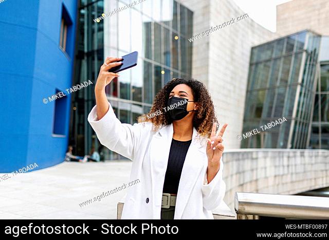 Woman taking selfie through smart phone against building during COVID-19