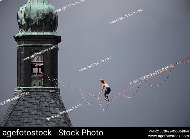 28 August 2021, Saxony, Hohnstein: A slackline runner balances on a rope between the castle and the town church of the town in Saxon Switzerland at the Highline...