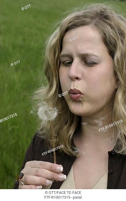 Young woman blowing dandelion seeds, close-up