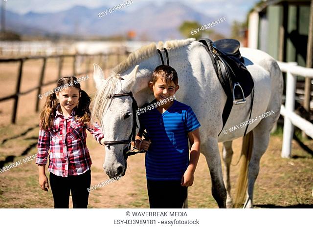 Siblings standing with white horse in the ranch