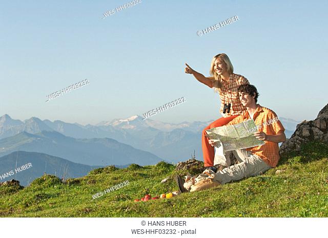 Young couple sitting on mountaintop, man holding map, smiling
