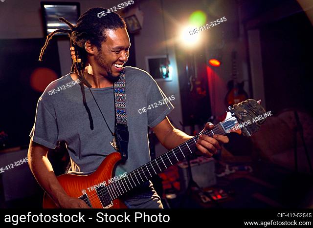 Happy male musician playing electric guitar in recording studio
