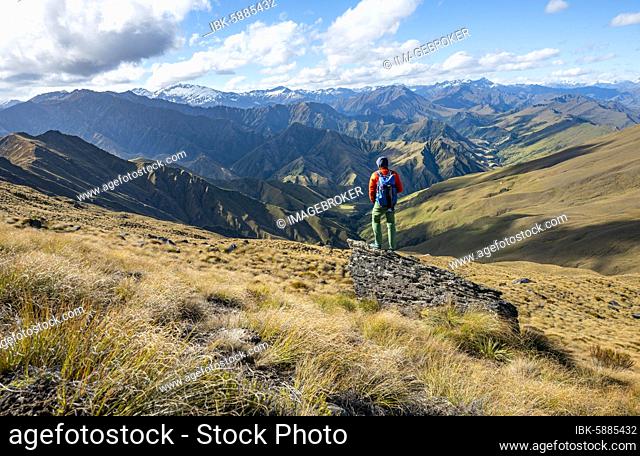 Hiker stands on stone, hiking trail to Ben Lomond, view of mountains, Southern Alps, Otago, South Island, New Zealand, Oceania