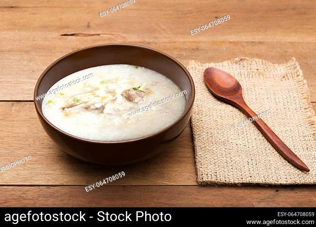 Traditional chinese porridge rice gruel in brown bowl with wooden spoon on wood table