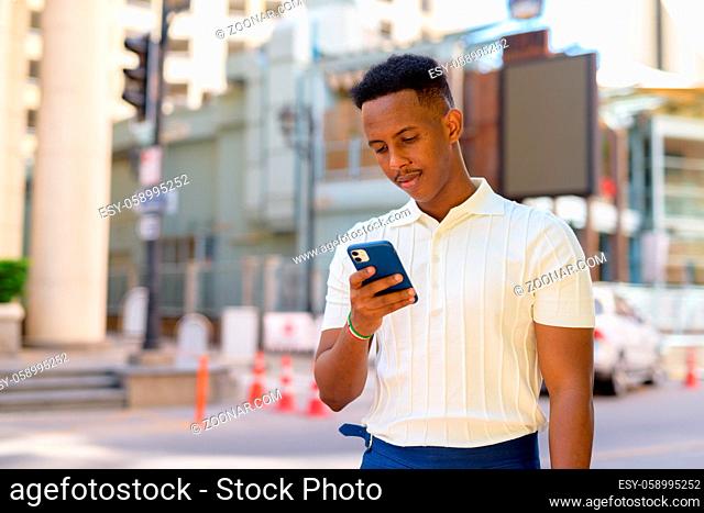 Portrait of confident young African businessman wearing casual clothes and using mobile phone