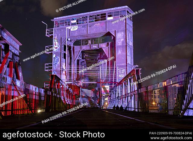 09 September 2022, Saxony-Anhalt, Magdeburg: Magdeburg's lift bridge is illuminated by colorful spotlights. Next to the bridge, a landmark of the city