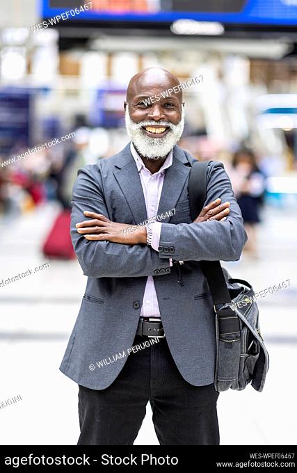 Smiling businessman with arms crossed carrying laptop bag at railroad station