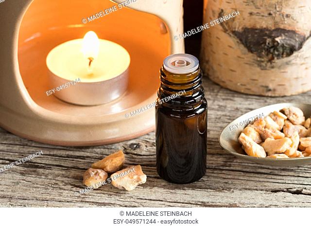 A bottle of styrax benzoin essential oil with styrax benzoin resin and a candle in the background