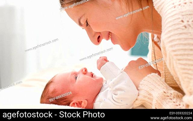 Closeup portrait of smiling loving mother stroking and looking on her newborn baby son lying on bed on bright sunny day. Concept of family happiness and loving...