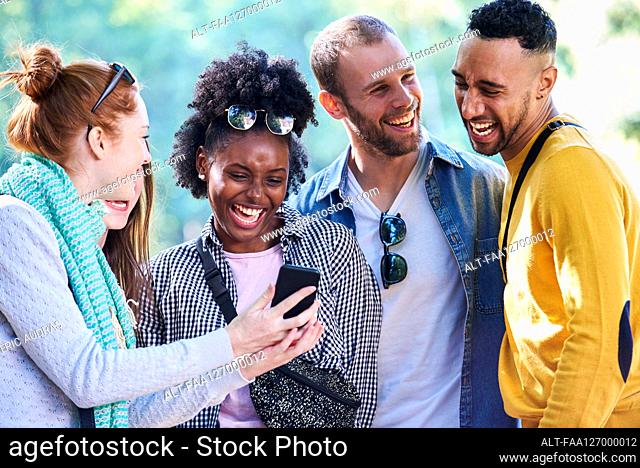 Happy young friends using smartphone in public park