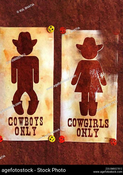 Partially faded toilet sign in a dude ranch. Male and female are depicted as cowboys and cowgirls wearing hats, Nova Scotia, Canada