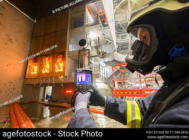 PRODUCTION - 10 October 2023, Lower Saxony, Brunswick: A firefighter checks a burning wooden façade with a thermal imaging camera during a research project at...