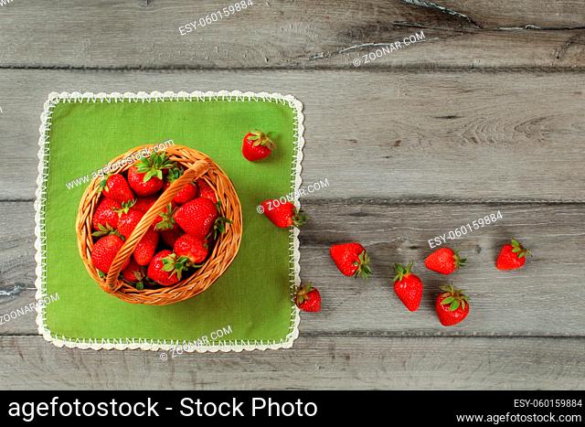 Tabletop photo, basket with strawberries , some of them spilled on green tablecloth and gray wooden desk