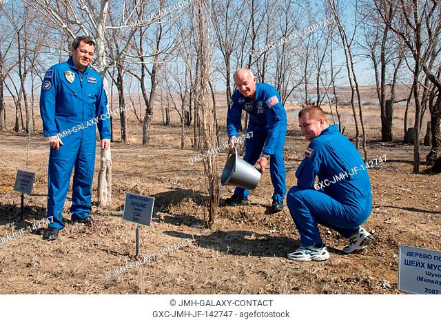 Behind the Cosmonaut Hotel crew quarters in Baikonur, Kazakhstan, Expedition 47-48 crewmember Jeff Williams of NASA (center) waters a tree previously planted in...