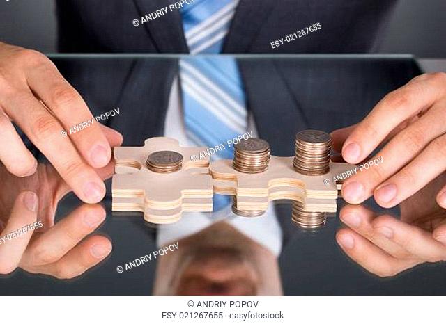 Hands connecting puzzle pices with coins