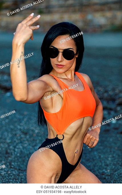 Fitness girl posing in the beach with a beautiful black and orange bikini and sunglasses