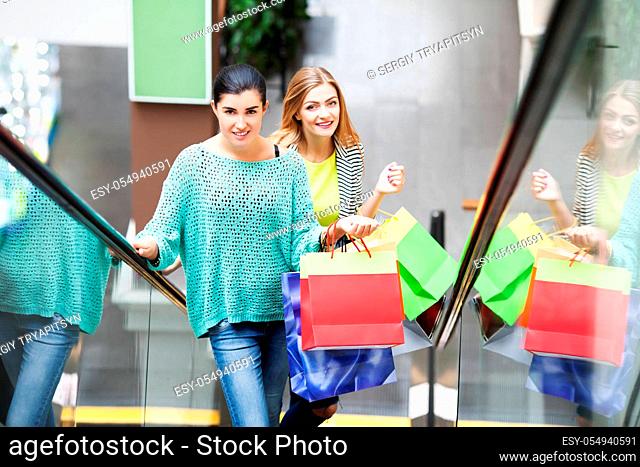 Women on the moving staircase holding bags after shopping