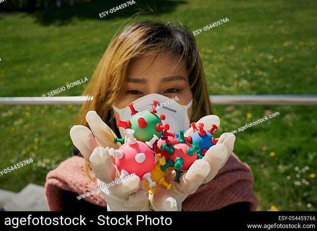 Asian woman with a protective mask and virus models on her hands. The concept of Coronavirus