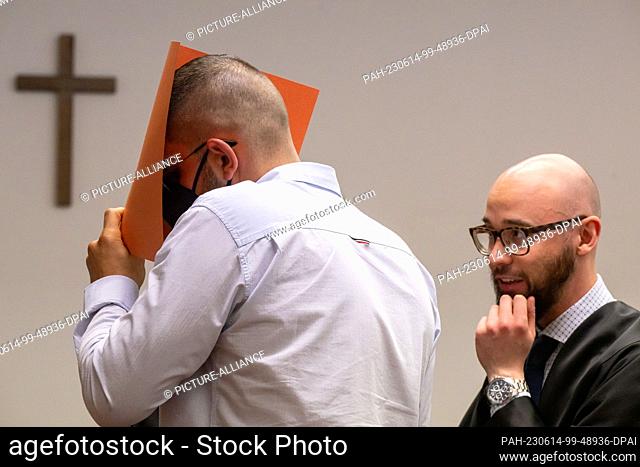 14 June 2023, Bavaria, Munich: The defendant covers his face with a file cover in the courtroom. His lawyer Deniz Aydin is on the right