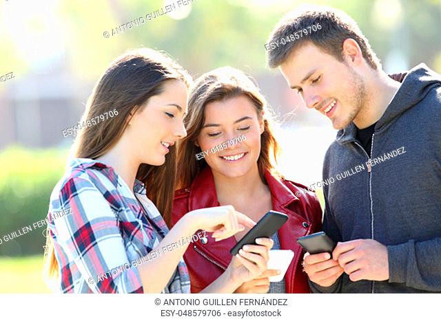 Three friends standing and sharing on line content with their smart phones in the street