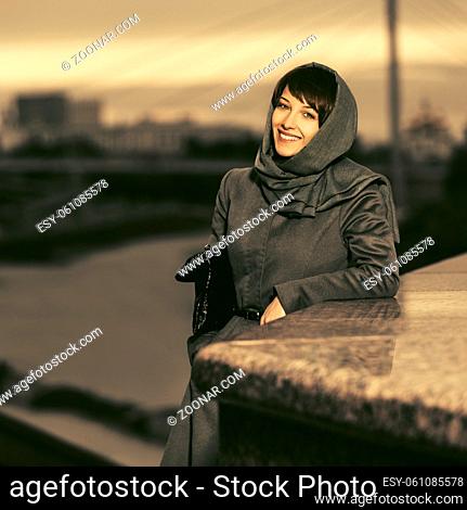 Happy young fashion woman in classic coat and headscarf walking outdoor