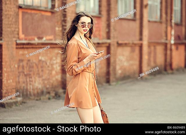 Beautiful young woman with earphones walking on the sidewalk