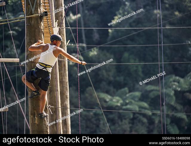 Man standing at top of poll ready to balance on suspended rope at outdoor ropes course