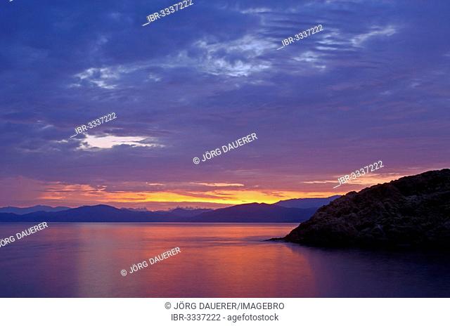 The rising sun forms sun beams behind the rocks of the island Ile de la Pietra near L'Île-Rousse. L'Île-Rousse is in the department Haute-Corse
