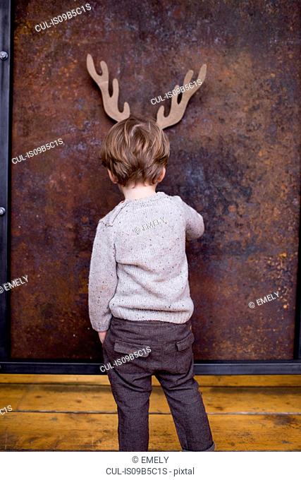 Young boy standing facing wall, cardboard reindeer cut out on wall behind him