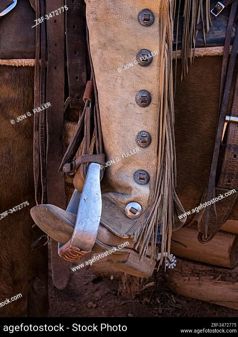 Close up detail of a cowboy's boot in a saddle stirrup with leather chaps and fringe. The leather chaps protect the cowboy's legs from thorny brush on the range