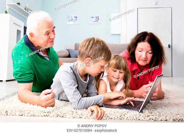 Family Playing Game On Laptop Computer Lying On Carpet At Home