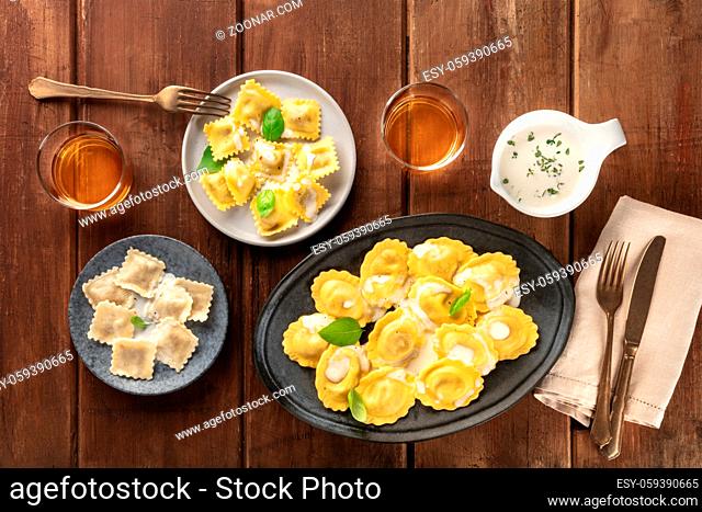 Italian Food. An assortment of various ravioli, shot from the top with glasses of wine and a white sauce on a dark rustic wooden background