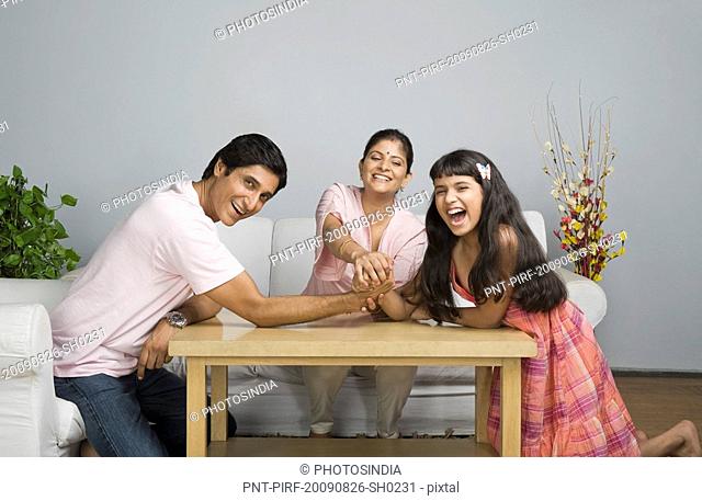 Portrait of a girl arm wrestling with her father and her mother supporting her