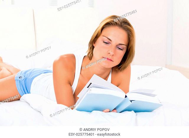 Young Woman Reading Book While Lying In Bed
